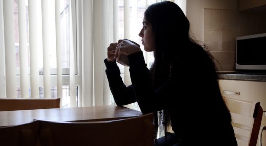 A woman sat at a table holding a mug looking out of the window.