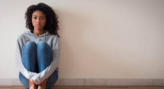 A young women sit on the floor holding her knees looking anxious