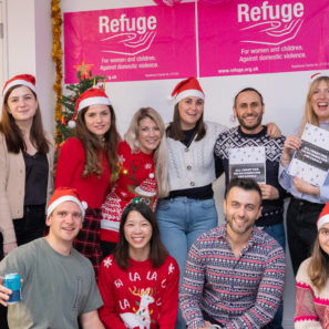 A group of staff wearing Santa hats and Christmas jumpers in front of a Refuge banner