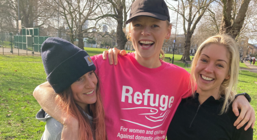 Image of three women in a park. One in the middle is wearing a Refuge t-shirt.