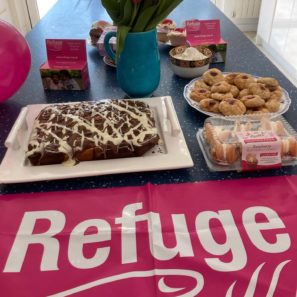 Image of a table with baked goods on it, some flowers and a Refuge banner