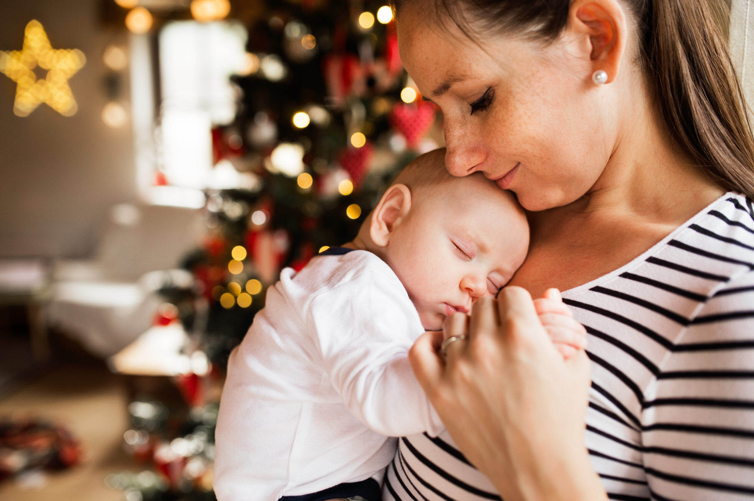 A women holds a sleeping baby with A Christmas tree in the bakground