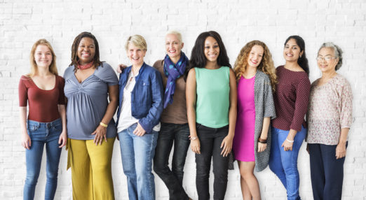 Diverse group of 8 women standing against a white wall looking into the camera