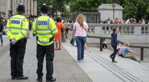 Two police officer wearing Met police jackets stand in Trafalgar square. They are male but not identifiable.