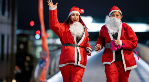 Two women dressed in Santa outfits walking at night