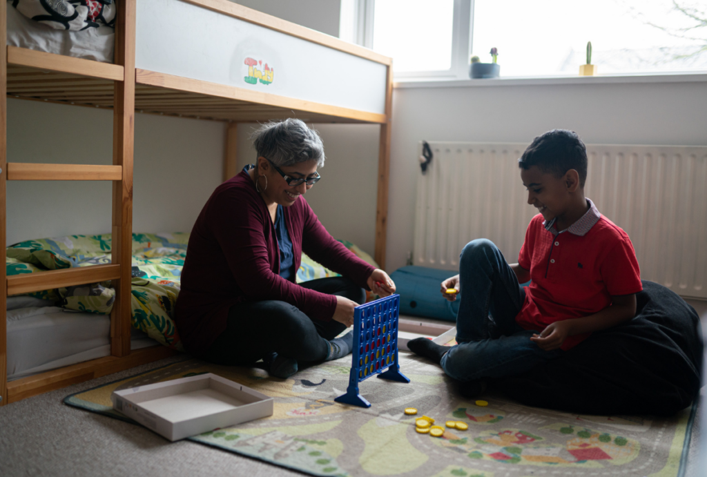 Mother and son sat on the floor of a child's bedroom playing connect four