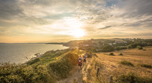 A group of people hike along a coastal path at sunset