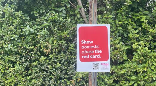 Poster reading 'give domestic abuse the red card' pinned outside to lamppost