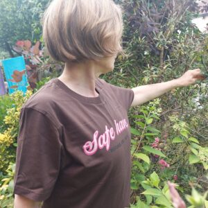 Woman stood outside in a t-shirt rwhich reads 'safe haven'. She is turned away from camera, her hand out towards nature.
