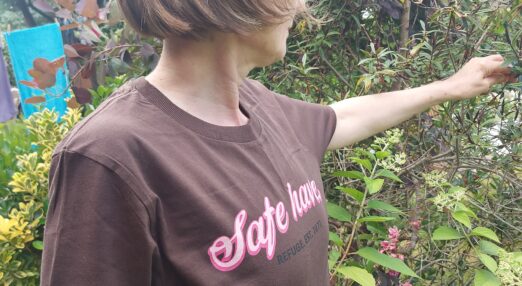 Woman stood outside in a t-shirt rwhich reads 'safe haven'. She is turned away from camera, her hand out towards nature.