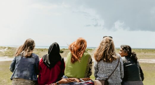Five women sat in a row, outside in nature, with their backs to camera
