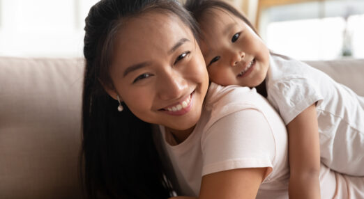 Vietnamese mother and daughter in their home, grinning at camera